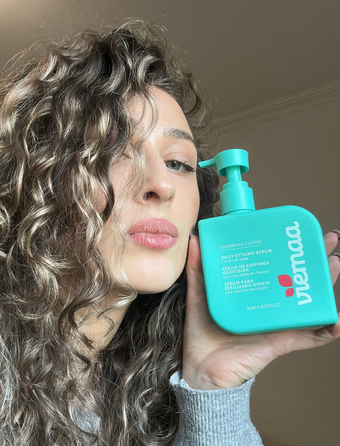 A woman with gorgeous curls holding up a viemaa daily styling serum bottle. 