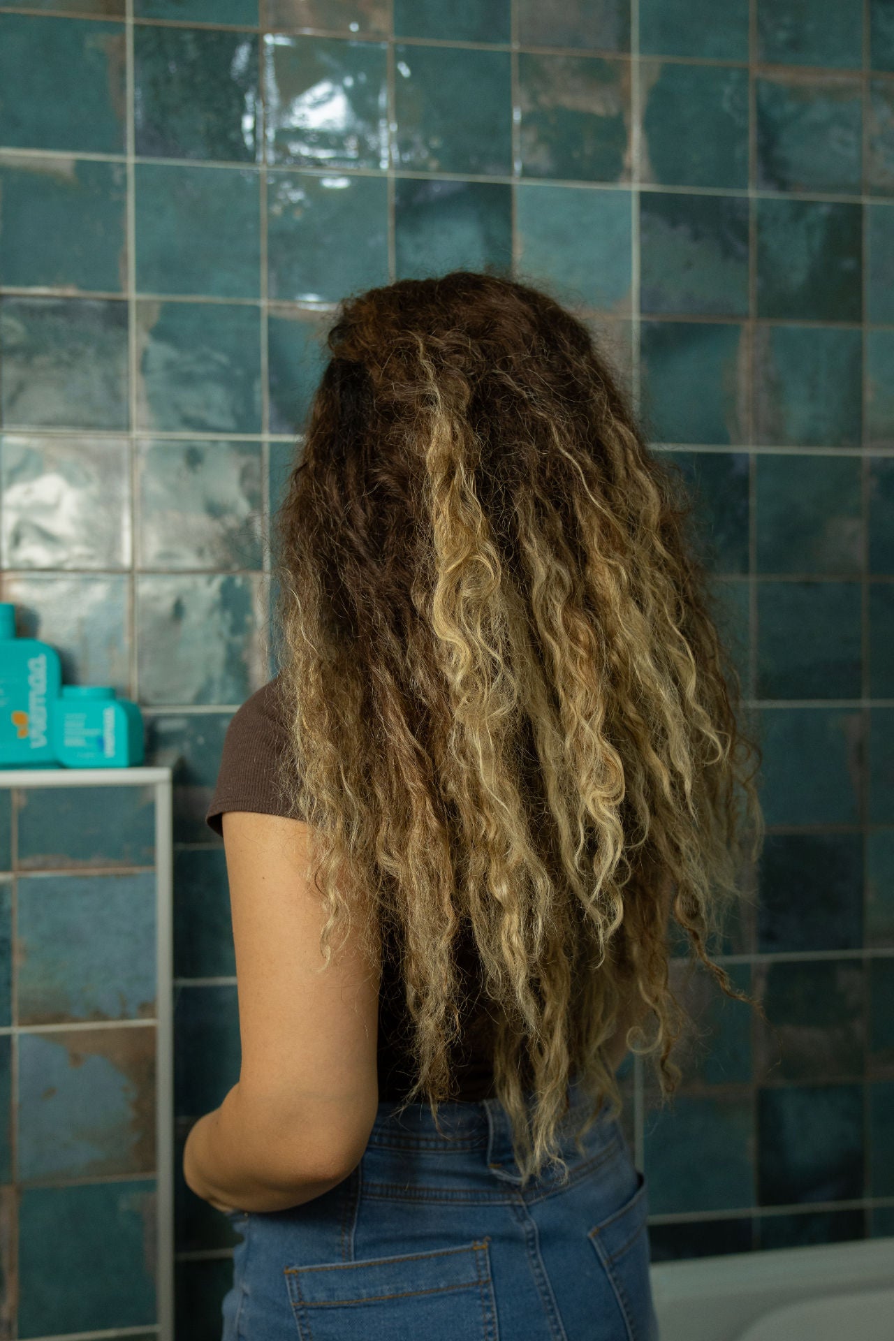 A woman with frizzy hair with her back to the camera considers viemaa's frizzy hair treatments. 