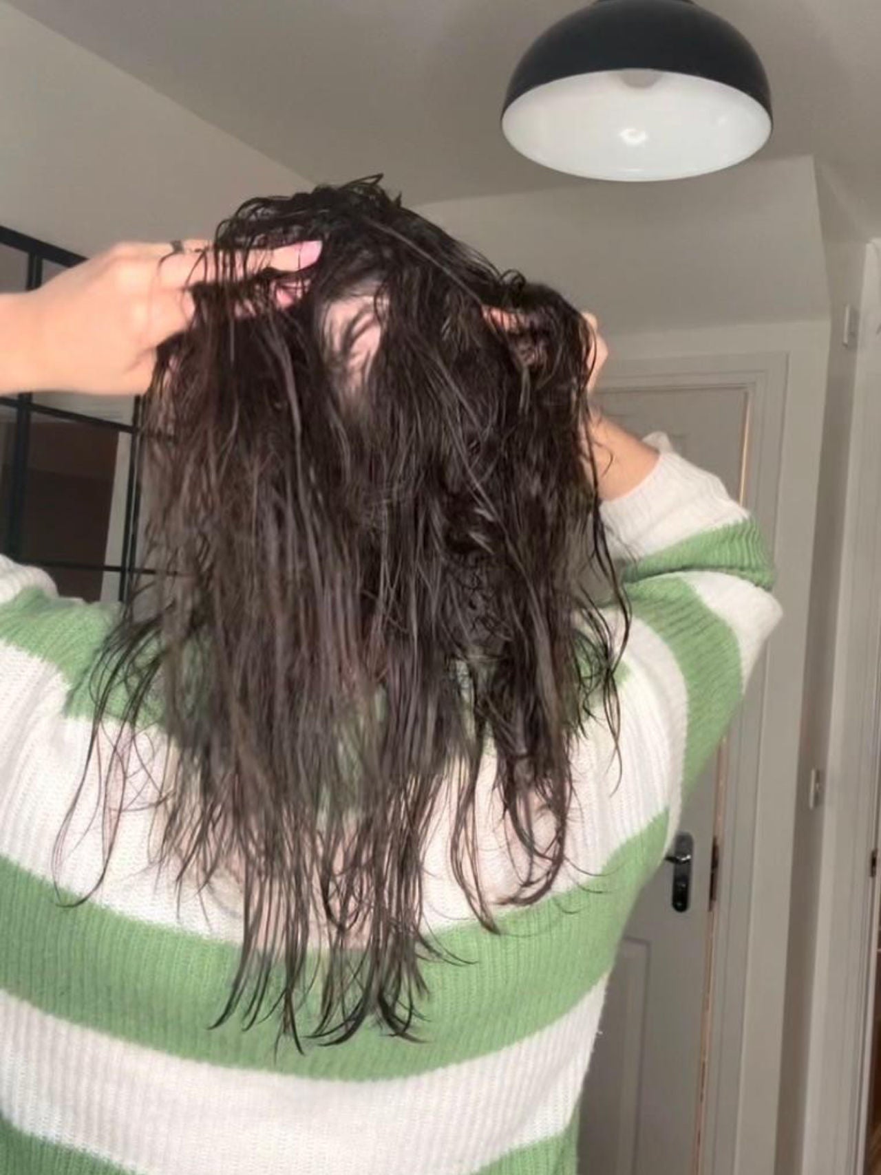 A woman parts her hair behind her head to show how she's experiencing hair thinning and hair loss. 